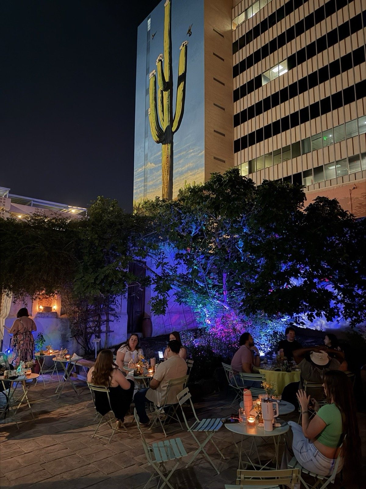 Mesas del patio a la luz de las velas bajo el mural del saguaro / Candlelit courtyard tables beneath the saguaro mural